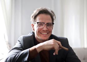 Cheerful businessman in glasses and suit holding a cigar, indoors.